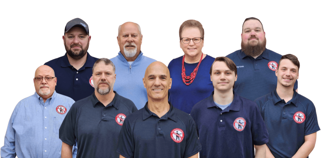 Group photo of the Security Zone Inc. team featuring nine members. Individuals are dressed in navy and light blue shirts with company logos, standing together in two rows and smiling. Background has been removed for a transparent effect.